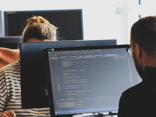 Two developers reviewing code on large monitors in a bright office